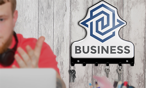 Person in red shirt at laptop, headphones on neck; wall key holder with BUSINESS logo and hanging keys