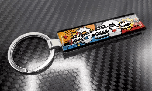 Llavero XL delgado estilo cómic con un diseño colorido de matrícula sobre una superficie con textura de carbono