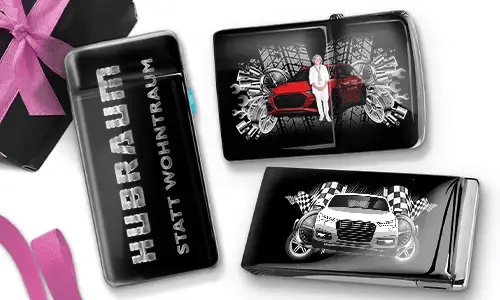 Drei Zigarettenetuis in Schwarz und Silber mit dynamischen Auto-Grafiken. Eines trägt die Aufschrift „Hubraum statt Wohntraum“, während die anderen Rennmotive zeigen.