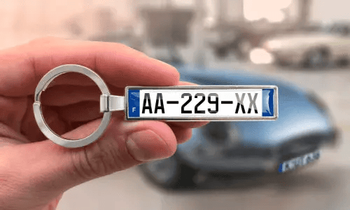 Brelok z niestandardową tablicą rejestracyjną, trzymany w ręce, z samochodem w tle
