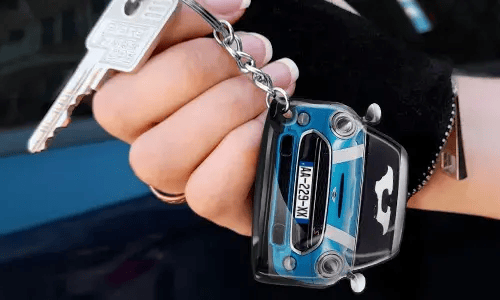 Hånd som holder en nøkkelring formet som en blå bil med detaljert frontdesign