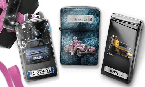 Three metal lighters featuring personalized designs. The left lighter shows a city skyline and a couple beside a car with 'BESTE OMA DER WELT'. The middle lighter depicts a pink vintage car with 'HAB DICH LIEB OMA' above. The right lighter displays a blue car and a license plate. Pink ribbons add a gift-like context.