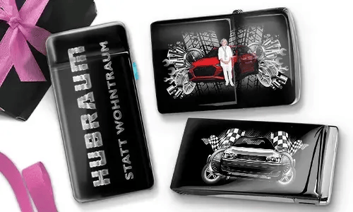 Drei Zigarettenetuis in Schwarz und Silber mit dynamischen Auto-Grafiken. Eines trägt die Aufschrift „Hubraum statt Wohntraum“, während die anderen Rennmotive zeigen.