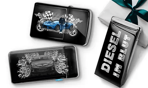 Two sleek black lighters featuring car themes, one with a blue car and checkered flags, another with a red car and gears. A third lighter reads 'DIESEL IM BLUT'. Gift-wrapped in the background.