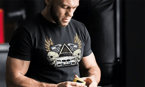 Black T-shirt with graphic of car, skulls, pistols, golden wings, and starry triangle background