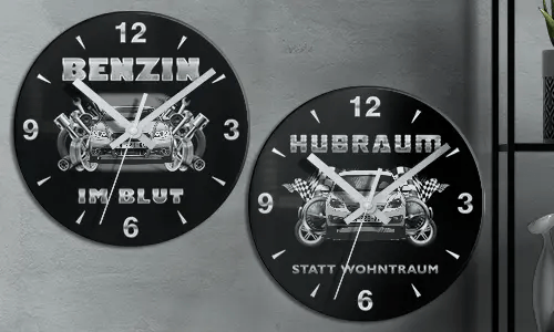 Zwei schwarze Wanduhren mit Autoillustrationen und deutschem Text: BENZIN IM BLUT und HUBRAUM STATT WOHNTRAUM
